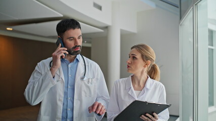Serious therapist talking mobile going clinic hallway with medical nurse closeup