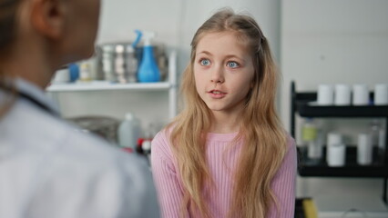 Cute girl visiting doctor in childcare clinic closeup. Pediatrician talking kid
