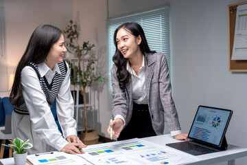 Two asian businesswomen analyzing charts on a desk with a computer