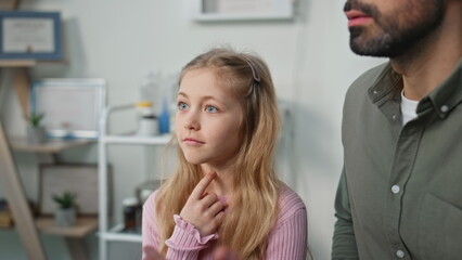 Child complaining sore throat in clinic closeup. Cute girl talk unknown doctor