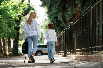Obraz premium Rear view, walking. Schoolgirl with her mother are outdoors together