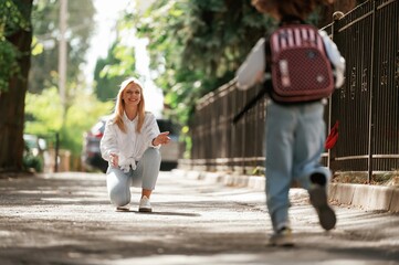 Obraz premium Meeting the girl after lessons. Schoolgirl with her mother are outdoors together