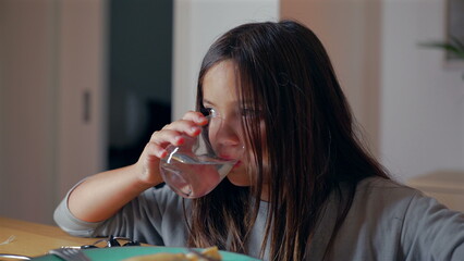 Young girl drinking water from a glass at the dining table, focusing on her concentrated expression...