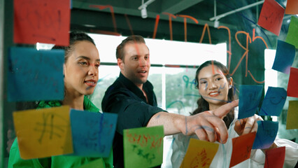 Portrait of professional diverse business team brainstorming marketing idea on colorful sticky notes stuck on glass board. Hispanic project manager write business strategy on note. Manipulator.