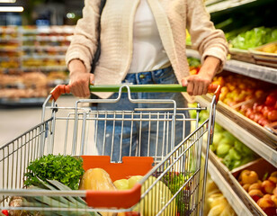 A young woman pushes a shopping cart in the supermarket in the fruit and vegetable section.