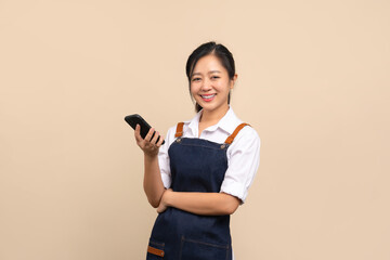 Naklejka premium Portrait of cute Asian girl in apron using smartphone on beige background