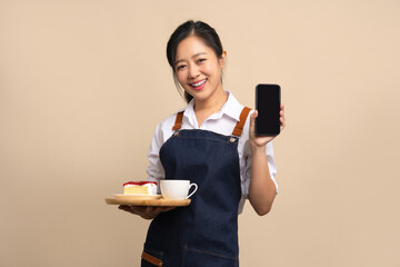 Asian female waitress in apron holding bread and coffee drink on wooden tray with smartphone on...