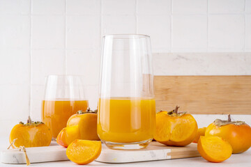Fresh homemade persimmon juice in portioned glasses, with whole and cut persimmon c in the...