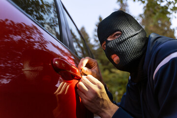 Masked thief breaking into a car with a lockpick