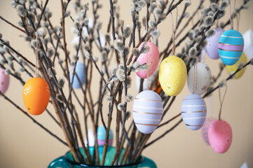 Decorative Easter eggs in various pastel colors hang on pussy willow branches arranged in a vase, creating a festive Easter centerpiece.