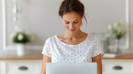 A young woman smiles while working on a laptop in a bright, modern kitchen, emphasizing a cozy and productive home environment.