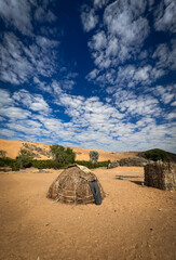 Traditional hut made of straw among sandy terrain in a village in Angola under a vibrant sky