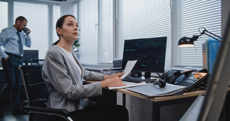 Workplace of managers of large financial company: Adult, beautiful female analyst checking data in paper documents for changes in foreign exchange rates. Monitoring stock and equity markets concept.