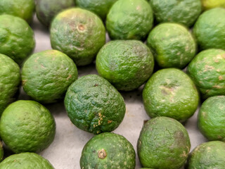 A close-up of a cluster of wrinkled green Citrus amblycarpa reveals their uniquely textured skins, covered in deep creases and folds. The limes' rich green color contrasts with their rugged.