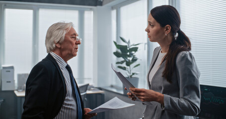 Obraz premium Two professional financial specialists holding paper documents discuss project ideas, brainstorm and develop business strategy. Senior boss and female employee have discussion in modern office.