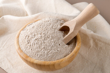 Buckwheat flour in a wooden bowl and raw buckwheat grain on cotton napkin on beige monochrome background. Alternative flour, gluten free flour, healthy nutrition