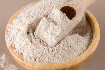 Buckwheat flour in a wooden bowl and raw buckwheat grain on beige monochrome background. Alternative flour, gluten free flour, healthy nutrition