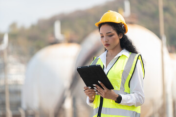 female engineer with hardhat with petrochemical factory background. asian woman holding tablet, plan and Walkie Talkie.