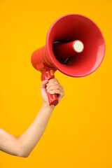Woman holding megaphone speaker on orange background, closeup