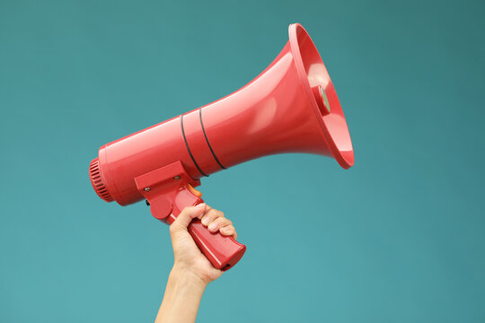 Woman holding megaphone speaker on blue background, closeup