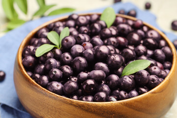 Ripe acai berries and leaves in bowl on table, closeup