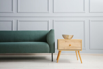 Stylish sofa and bowl on side table near grey wall