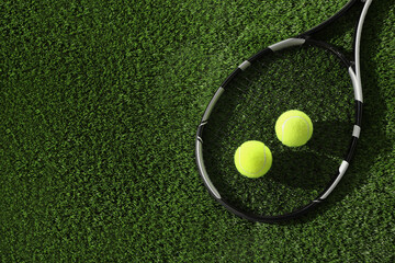 Tennis racket and balls on green artificial grass, flat lay. Space for text