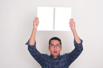 A man showing shocked and worried expression while holding empty book pages above his head