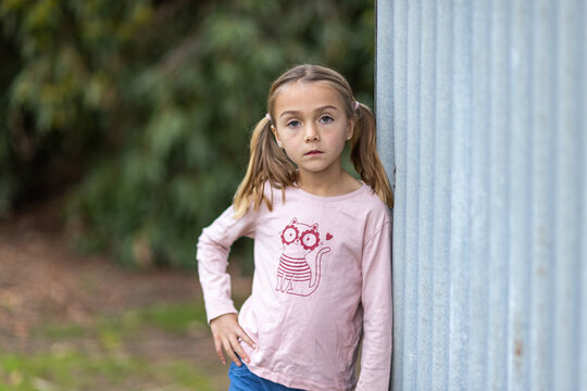 Young girl with a serious expression leaning on shed