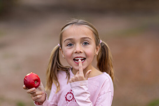 little girl pointing to wobbly tooth and holding an apple with a bite taken out of it