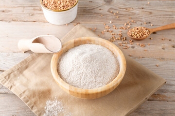 Buckwheat flour in a wooden bowl and raw buckwheat grain on cotton napkin on rustic wooden table background. Alternative flour, gluten free flour, healthy nutrition