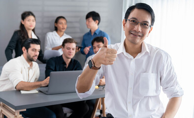 Confidence and happy smiling businessman portrait with background of his colleague and business team working in office. Office worker teamwork and positive workplace concept. Prudent
