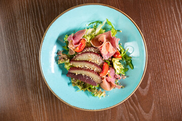 A gourmet salad featuring tomatoes and wine-marinated pear, elegantly presented on a blue plate. Ideal for themes of fine dining, healthy eating, and culinary artistry
