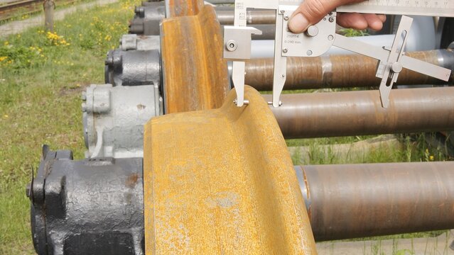 A technician measures train wheel to ensure safety, emphasizing precise work. Close-up of tools and techniques used for security testing. Ideal for projects focused on railway safety and maintenance.