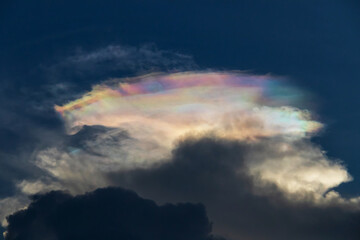 A stunning iridescent cloud formation against a dark sky, showcasing beautiful colors and striking...