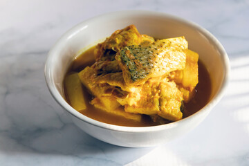 Yellow curry with fish and green taro (aaw dip) in hot pot on wooden table. Southern delicious food of Thailand.