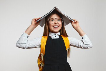 Happy student girl holding academic book on her head and looking away, wearing school uniform,...