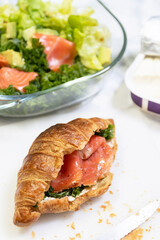 Delicious croissant filled with smoked salmon and greens, served with a side of salad for a healthy meal.