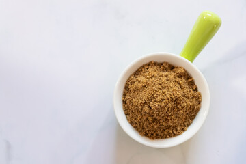 A close-up of brown sugar in a white ceramic bowl on a marble surface, highlighting its texture and natural sweetness.