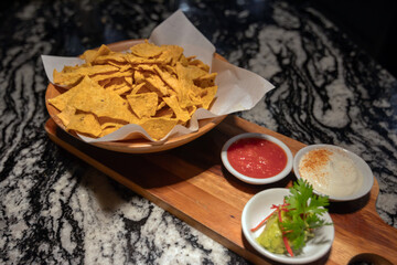 A delicious bowl of tortilla chips served with salsa, guacamole, and sour cream on a wooden platter.
