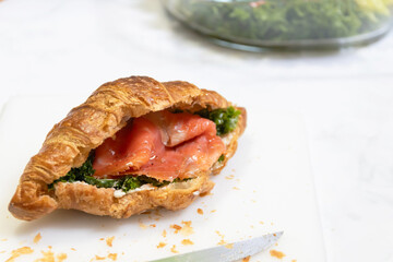 A delicious croissant filled with smoked salmon and greens, showcasing flaky pastry and vibrant ingredients for a delightful meal.