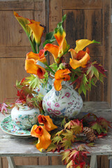 autumn still life of zantedeschia flowers in vases with maple leaves