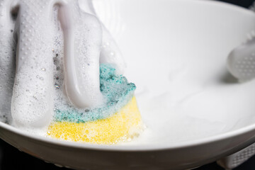 Hands wearing rubber gloves are washing dishes using a sponge,