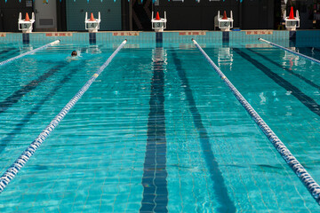 a mostly empty public swimming pool except for one person on a sunny day