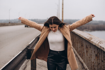 Smiling cheerful beautiful caucasian woman looking at the camera while walking on the bridge with hands raised