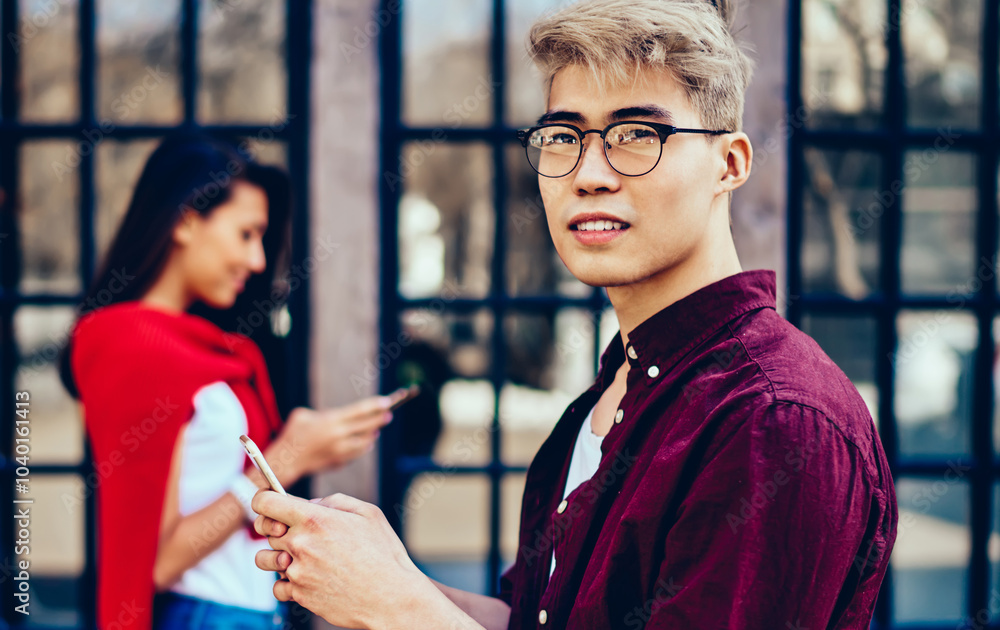 Poster pondering chinese hipster guy in eyeglasses looking away while messaging on smartphone and using 4g 