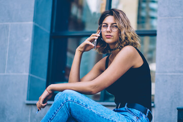 Portrait of beautiful female teenager looking at camera while calling to customer service for discussing details of roaming connection, young attractive hipster girl making telephone conversation