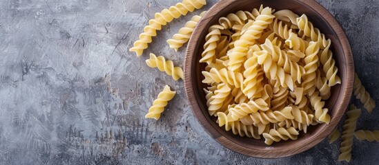 Wooden bowl with raw Creste di Gallo pasta on concrete background with space for additional image