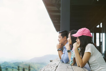 Parents and daughter sit with their hands under their chins looking at the mountain view outside from the balcony of their hotel accommodation during their vacation.Concept of family time and travel