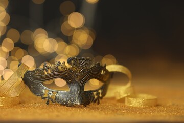 Beautiful carnival mask on golden shiny surface, closeup. Space for text